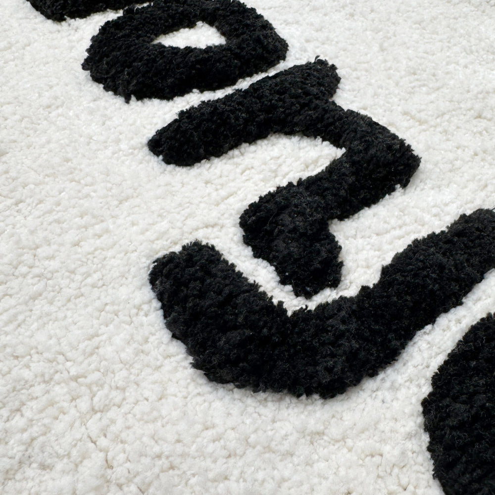Fluffy bath mat with bonjour slogan, white and black.