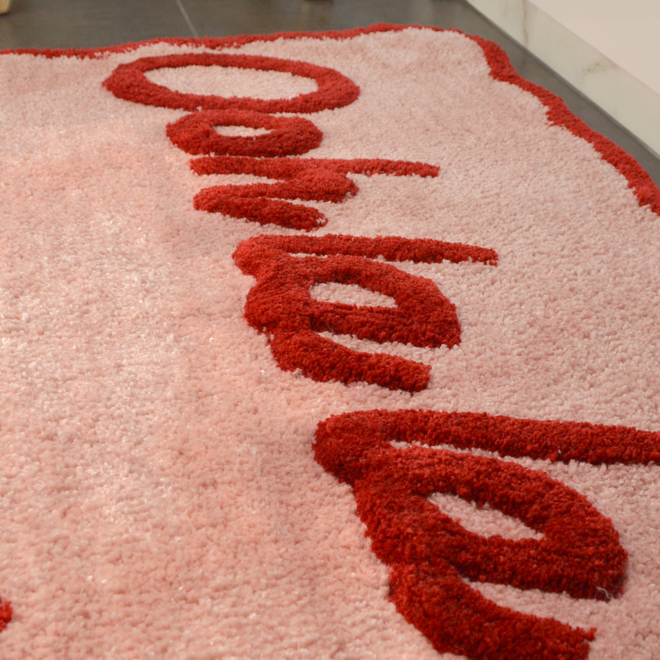 Pink and red bath mat with ooh la la slogan and scalloped shape.