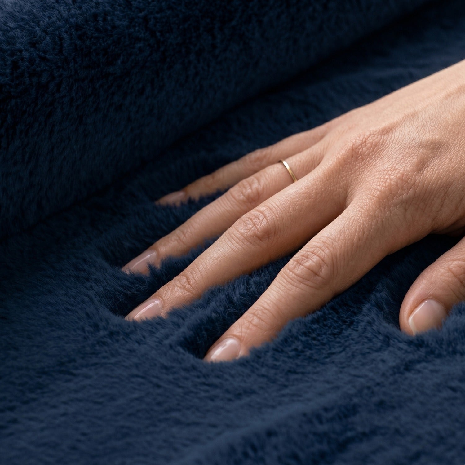 Hand with a ring on a navy blue softie rug pile