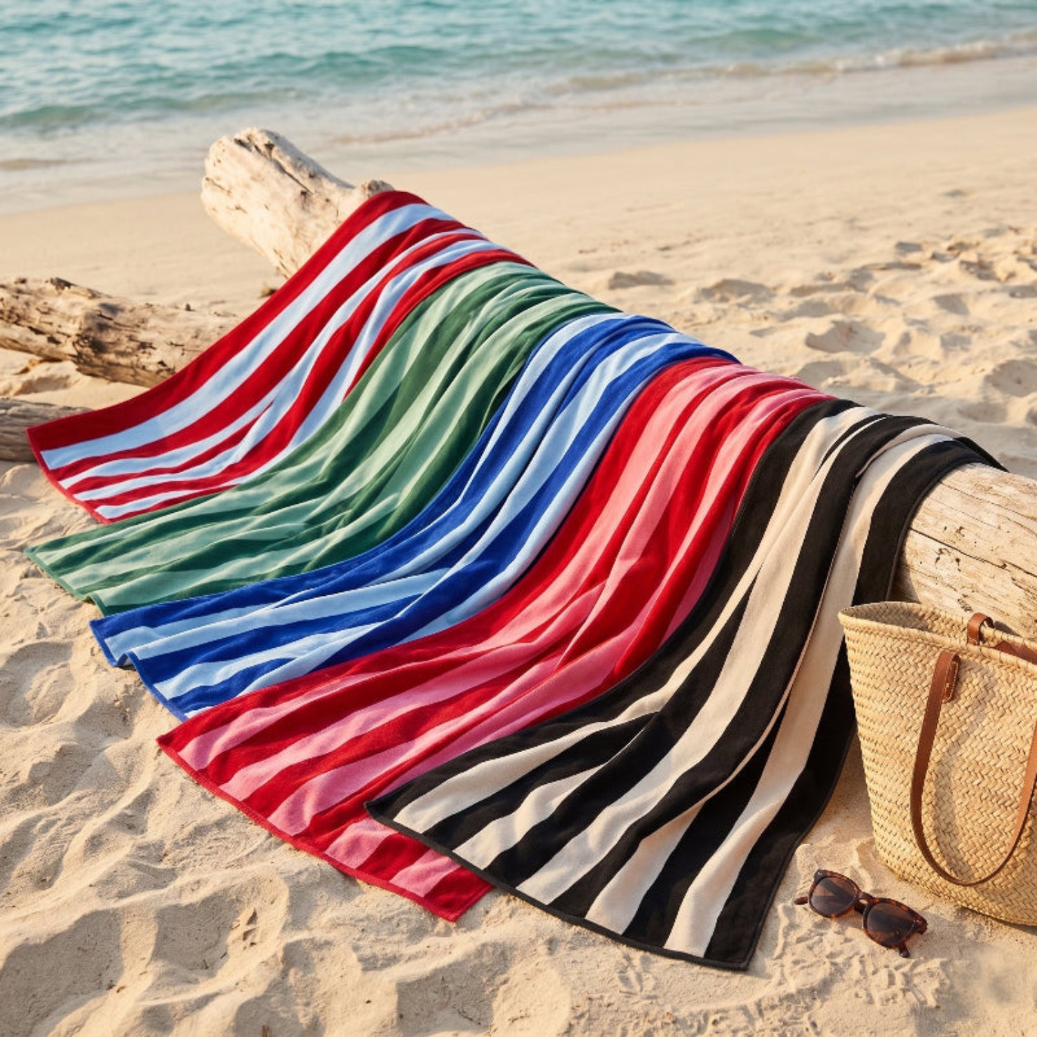 Colourful striped beach towels on a sandy beach with a straw bag and sunglasses.