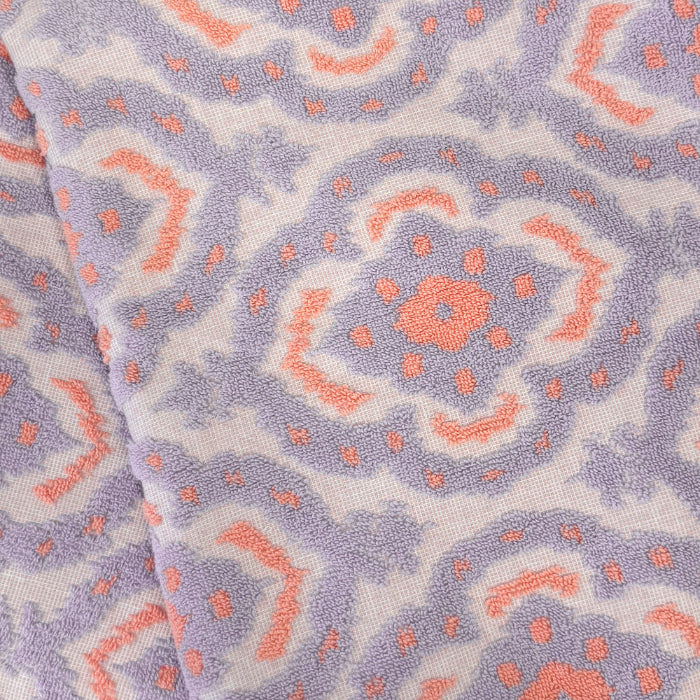 Close-up of cotton towel with a mandala pattern of pink and purple shapes on a white background.