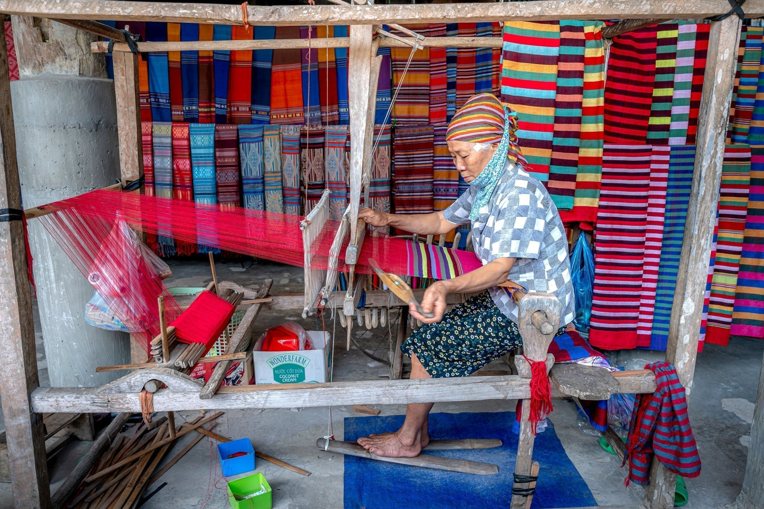 Senior woman artisan weaving intricate textiles on a wooden loom.