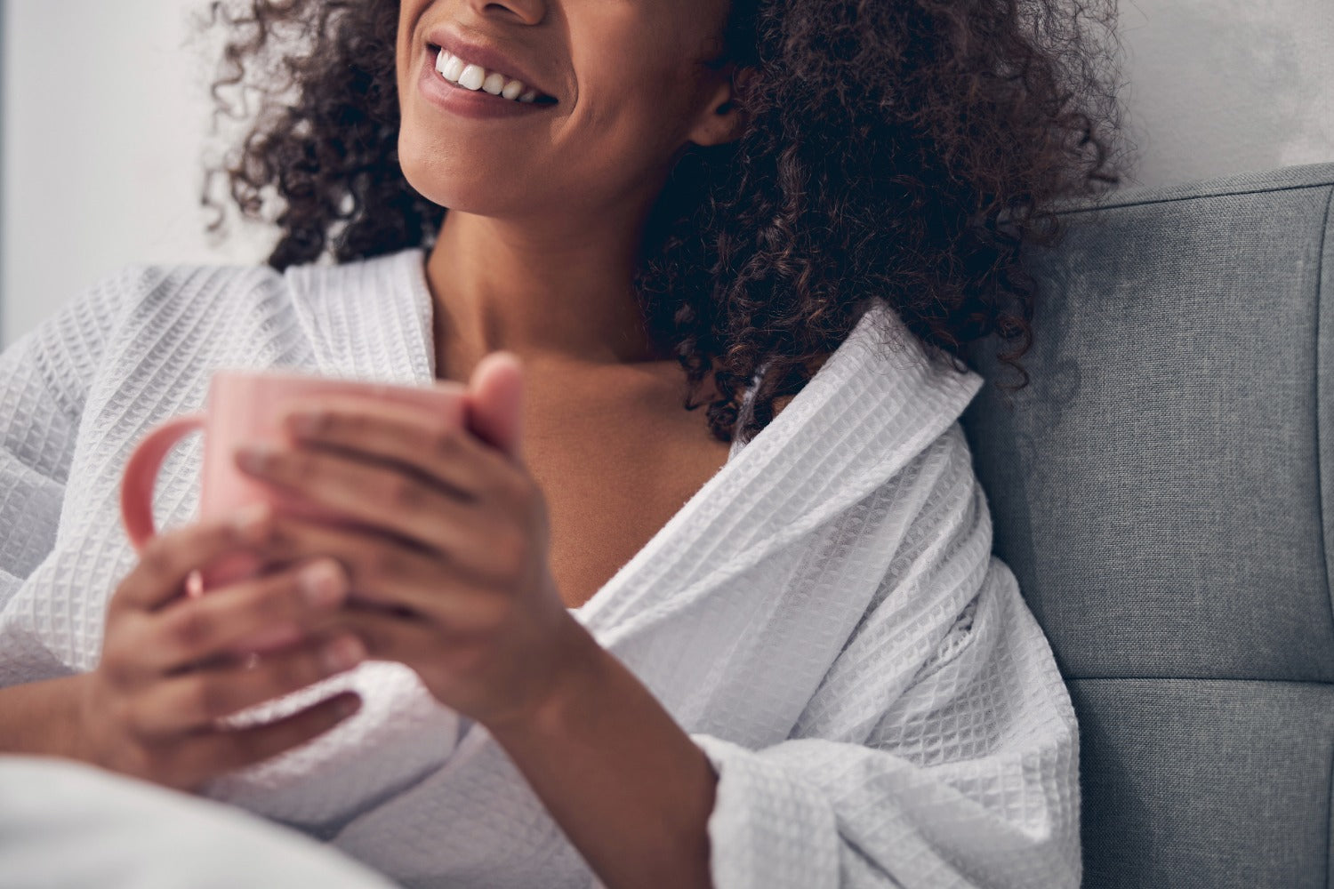 woman sat on a bed holding a mug wearing a waffle dressing gown