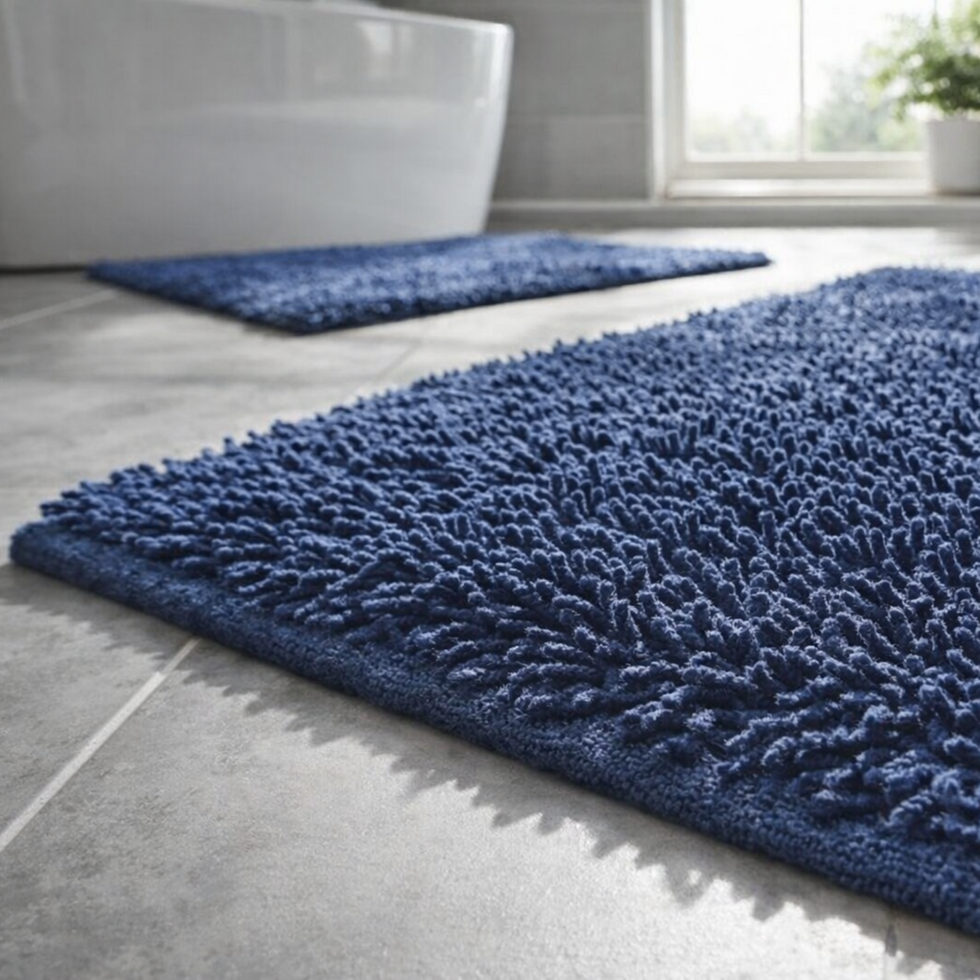 A dark blue shaggy bath mat in a bathroom setting, with a matching bath rug further in the background near a bathtub.