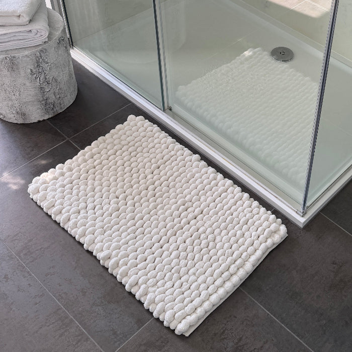 White textured bath mat on a bathroom floor with a shower in the background