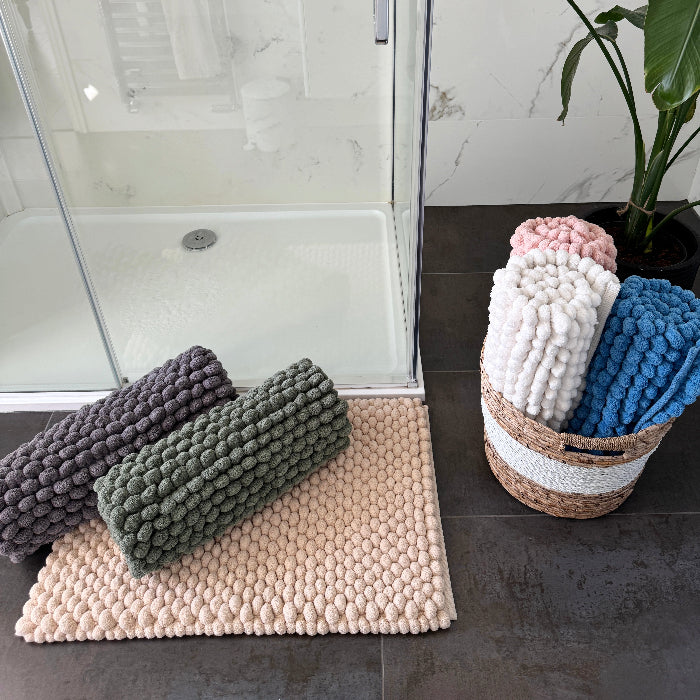 Giant bobble bath mats in various colours on a bathroom floor with a basket of additional mats.
