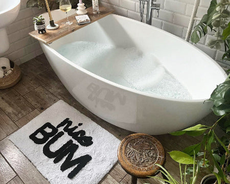 Bathroom with a white freestanding bathtub, wooden stool, slogan bath mat and decorative elements.