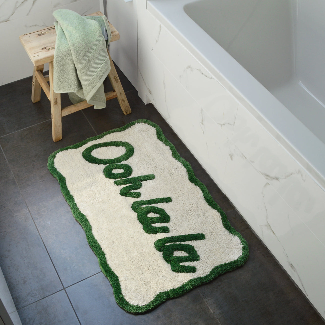 Green bath mat next to bathtub with ooh la la slogan, fun scalloped shape mat.