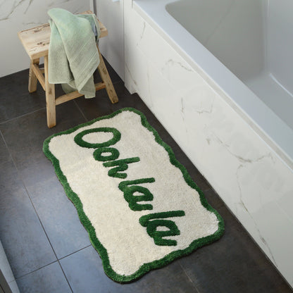 Green bath mat next to bathtub with ooh la la slogan, fun scalloped shape mat.