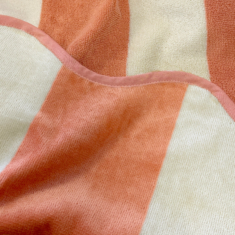 Close up of striped reversible beach towel with terry cloth and velour feel, burnt orange colour.