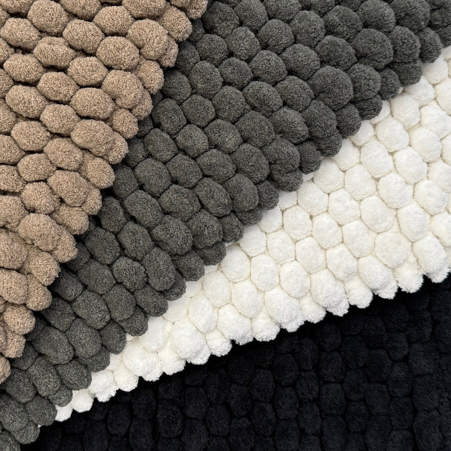 Close-up of textured bath rugs in beige, gray, white, and black.