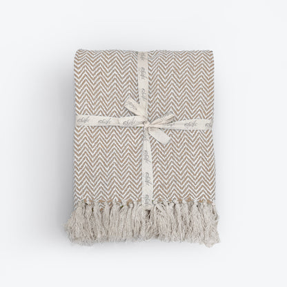 Beige throw blanket in herringbone chevron pattern. Neutral cotton throw for the sofa.