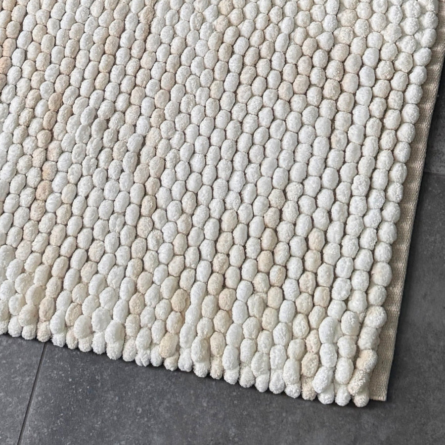 Cream and beige bath mat is marble pattern, handwoven deep pile bobbles.