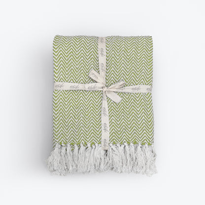 Green patterned blanket with fringe in herringbone chevron design.