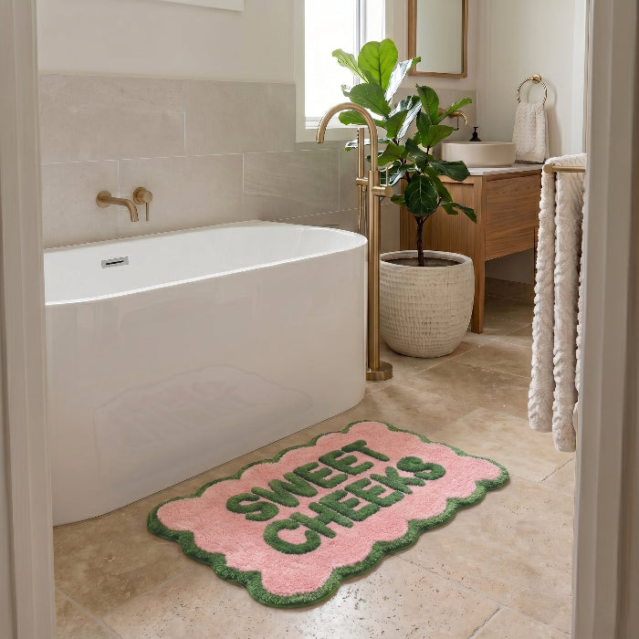 Pink and green bath mat with scalloped edges, sweet cheeks slogan.