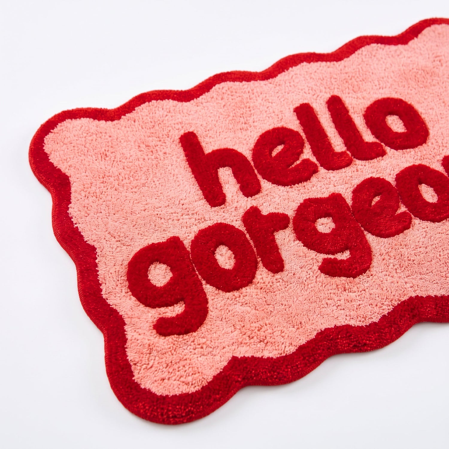 Red and pink bath mat with scalloped edges and hello gorgeous slogan.