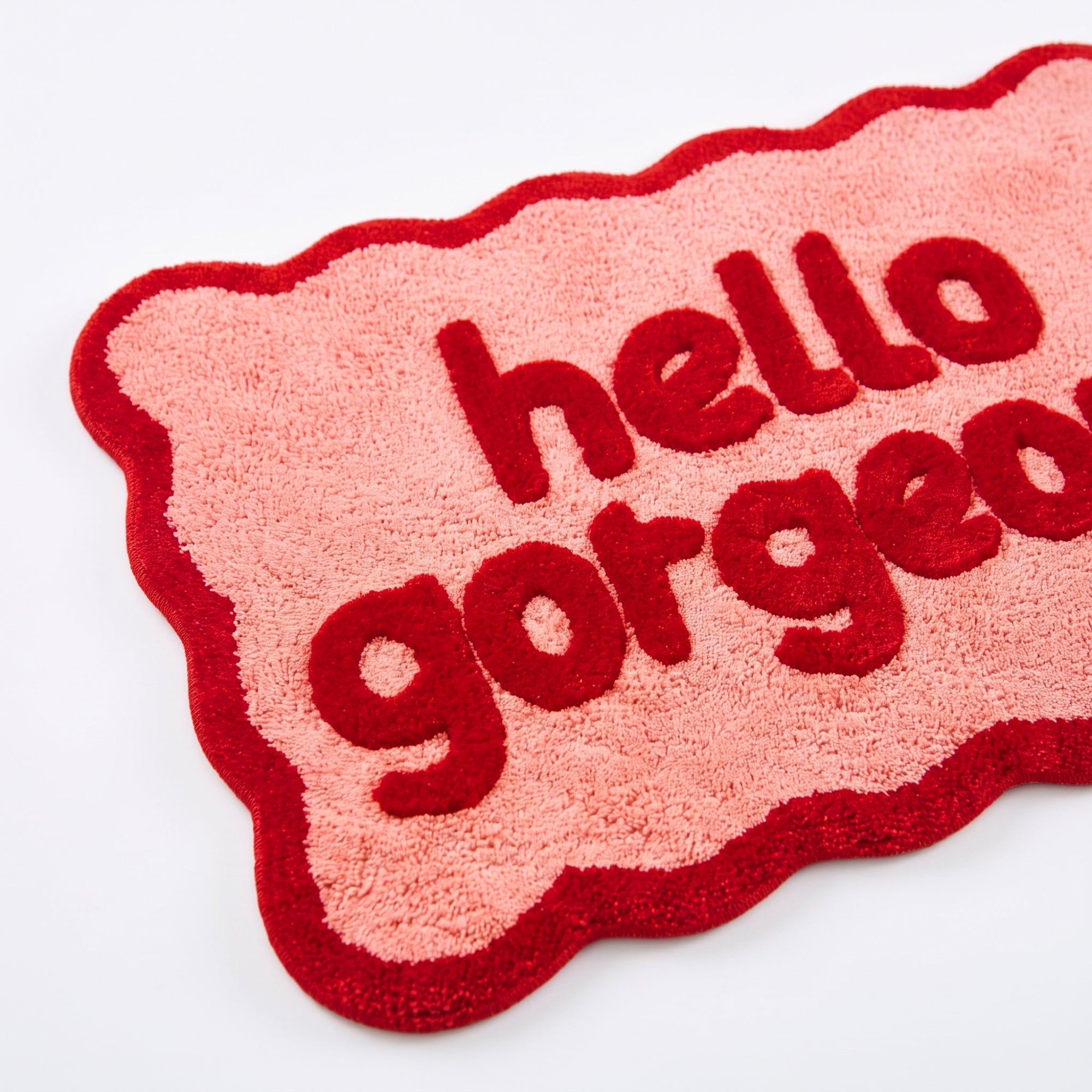Red and pink bath mat with scalloped edges and hello gorgeous slogan.
