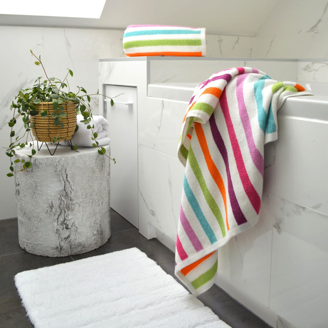 A set of vibrant multicolored striped towels displayed in a bathroom setting, with colors including pink, orange, green, and blue.