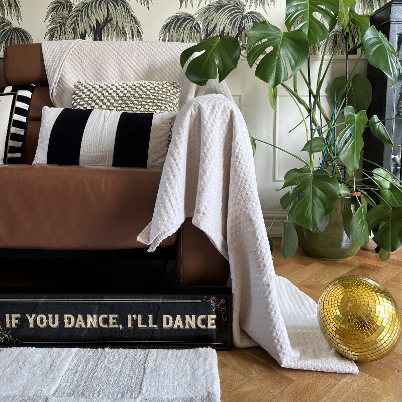 Living room with brown sofa, decorative pillows, white waffle blanket, and a gold disco ball.